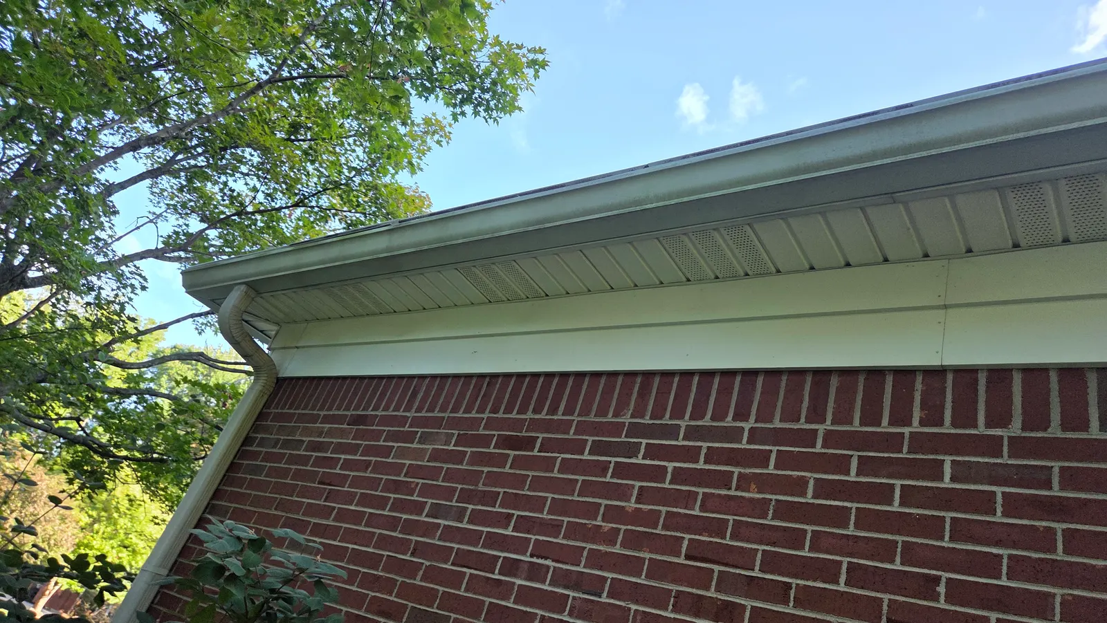 A clean white gutter, downspout and soffit on a brick house under a blue sky.