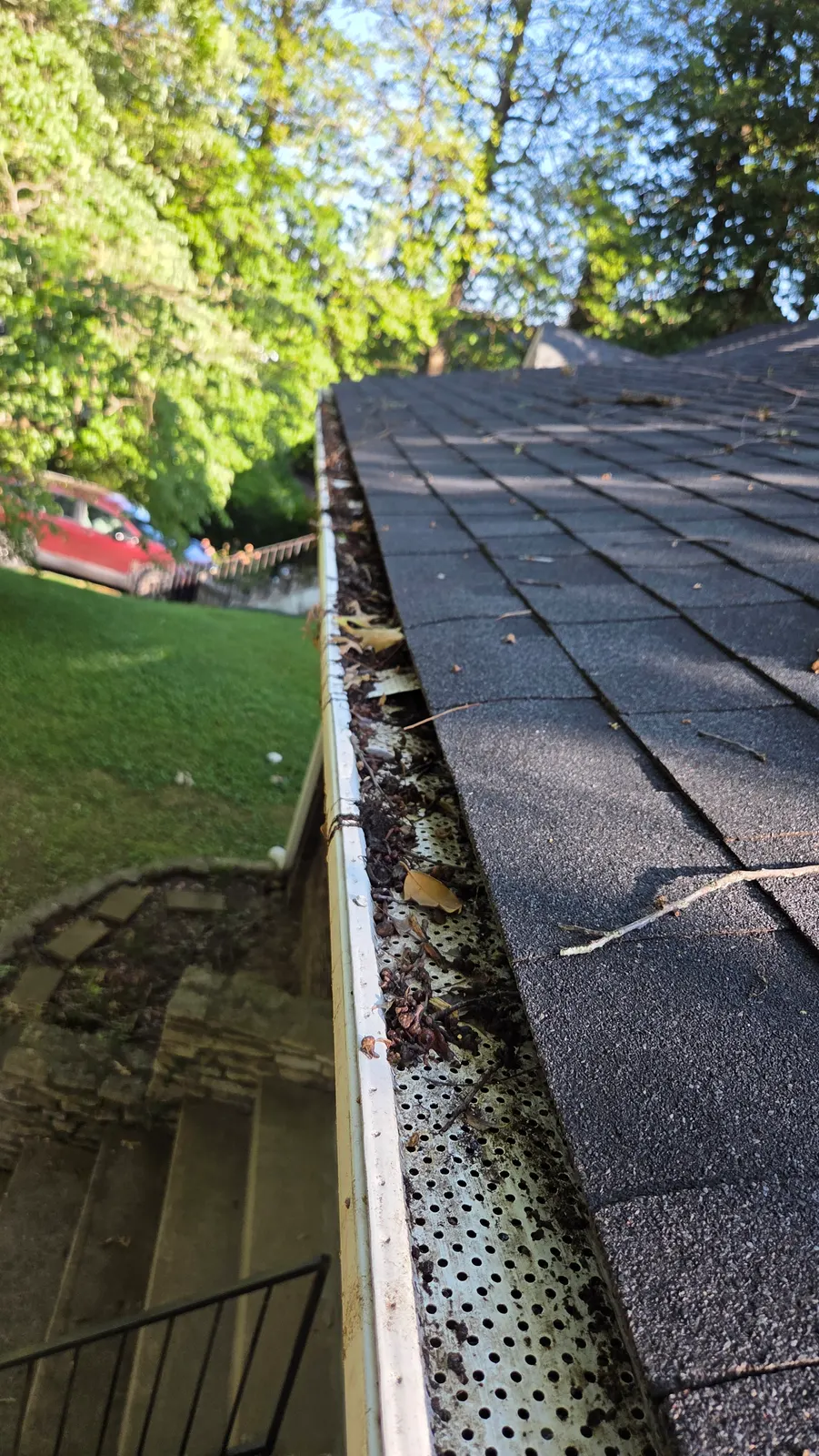 Leaves, twigs and debris sitting on top of a perforated gutter guard along the edge of a shingle roof.