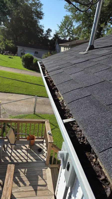 A roofline gutter packed with dark, wet leaves and debris, seen from the roof above a wooden deck.