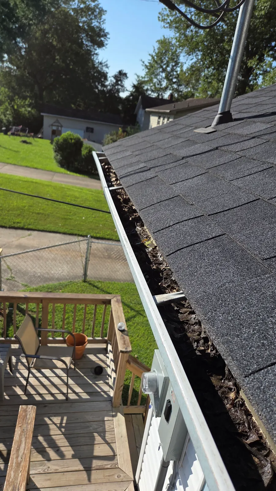 A roofline gutter packed with dark, wet leaves and debris, seen from the roof above a wooden deck.