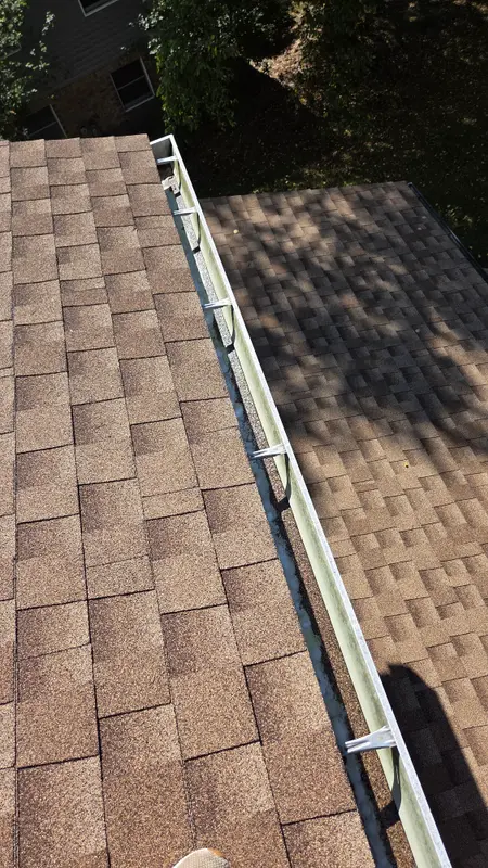 An empty, clean gutter running along the edge of a brown shingle roof in the sun.