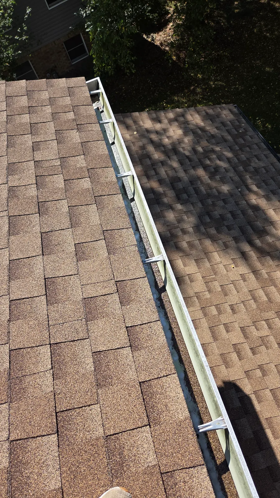 An empty, clean gutter running along the edge of a brown shingle roof in the sun.