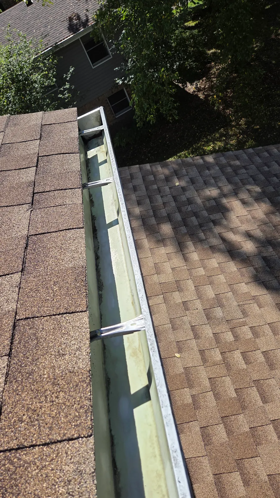 A cleared gutter along a brown shingle roof, empty down to the metal.