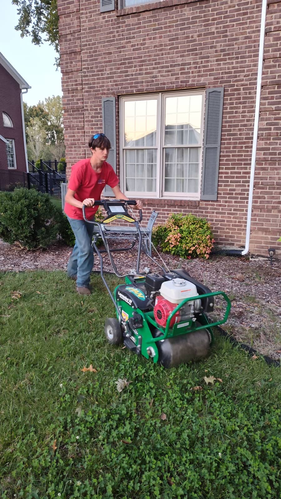 Elite Exteriors team member operating a core aerator across a green residential lawn in Floyds Knobs, IN