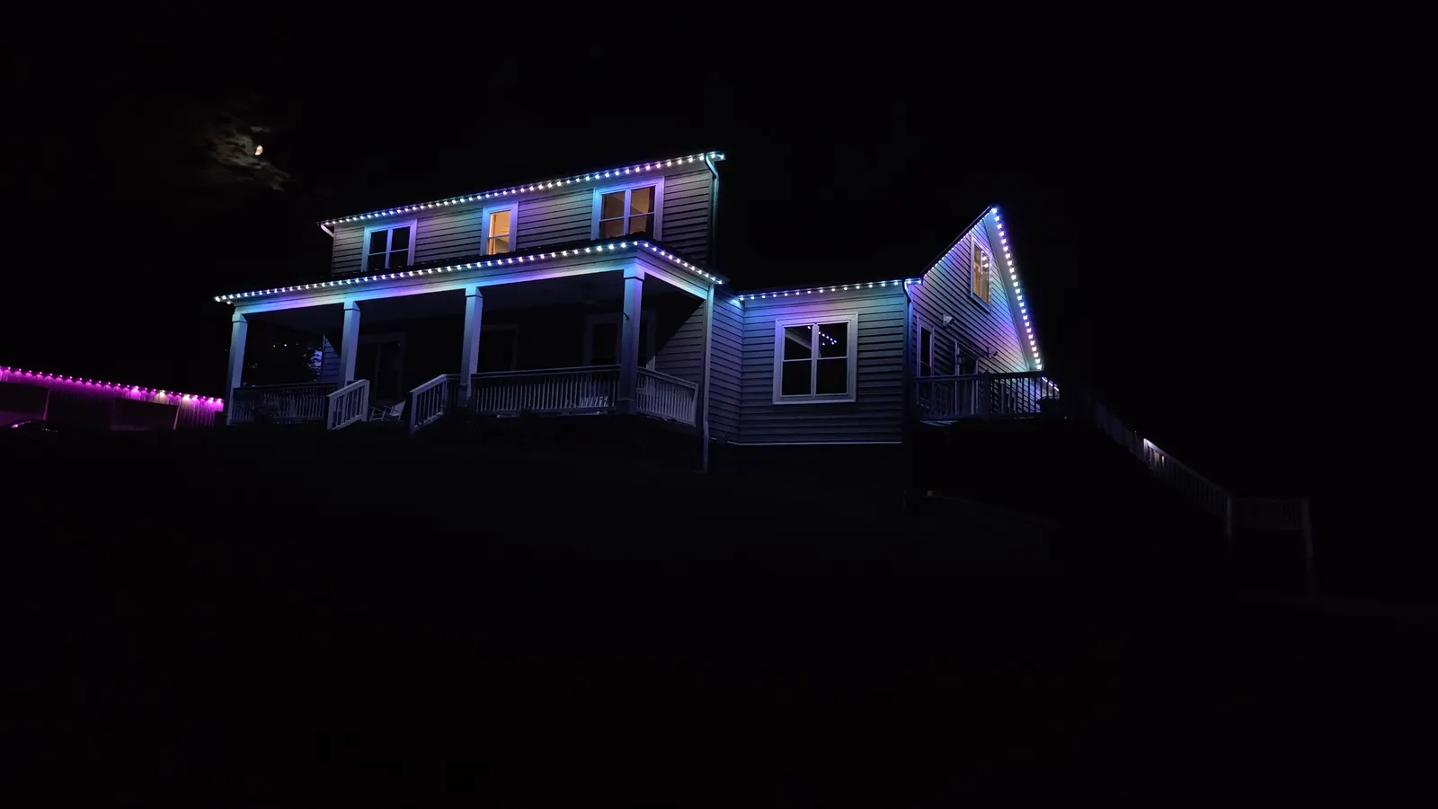 Angled night view of a two-story house and attached garage with rooflines outlined in blue and teal LED lights.