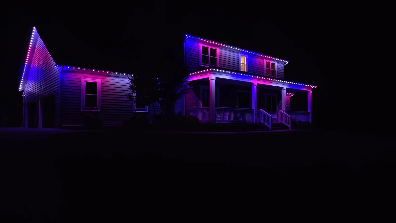 A two-story house and garage at night washed in pink and blue light from permanent LED roofline lighting.