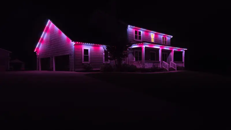 A two-story house and garage at night with rooflines lit in pink and white permanent LED lights.
