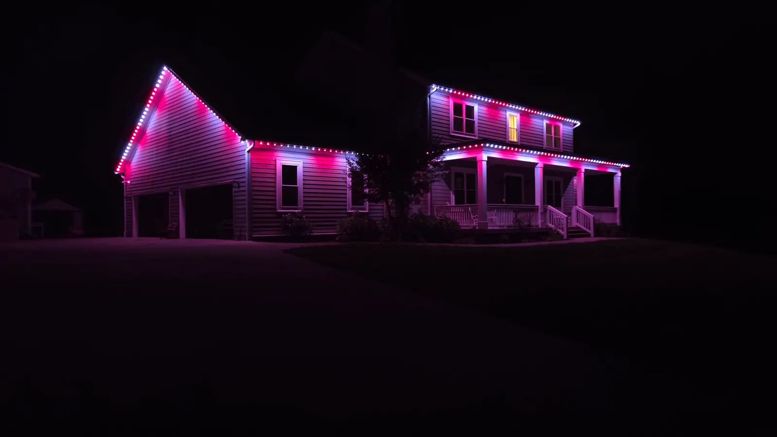 A two-story house and garage at night with rooflines lit in pink and white permanent LED lights.