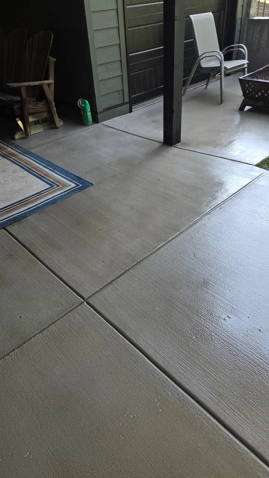 Covered concrete patio after pressure washing, clean and uniform, with patio chairs and an outdoor rug in the background.
