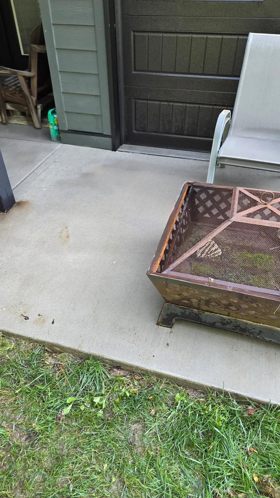 The same concrete slab in front of the dark garage door, clean and even in color, with a fire pit and chair set back on it.