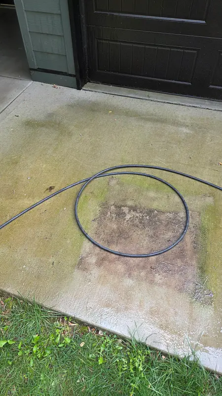 Concrete slab in front of a dark garage door covered in green algae, with a dark square stain where something had been sitting.