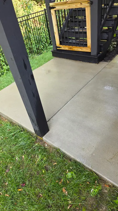 Clean light gray concrete patio beside a dark support post and a green lawn.