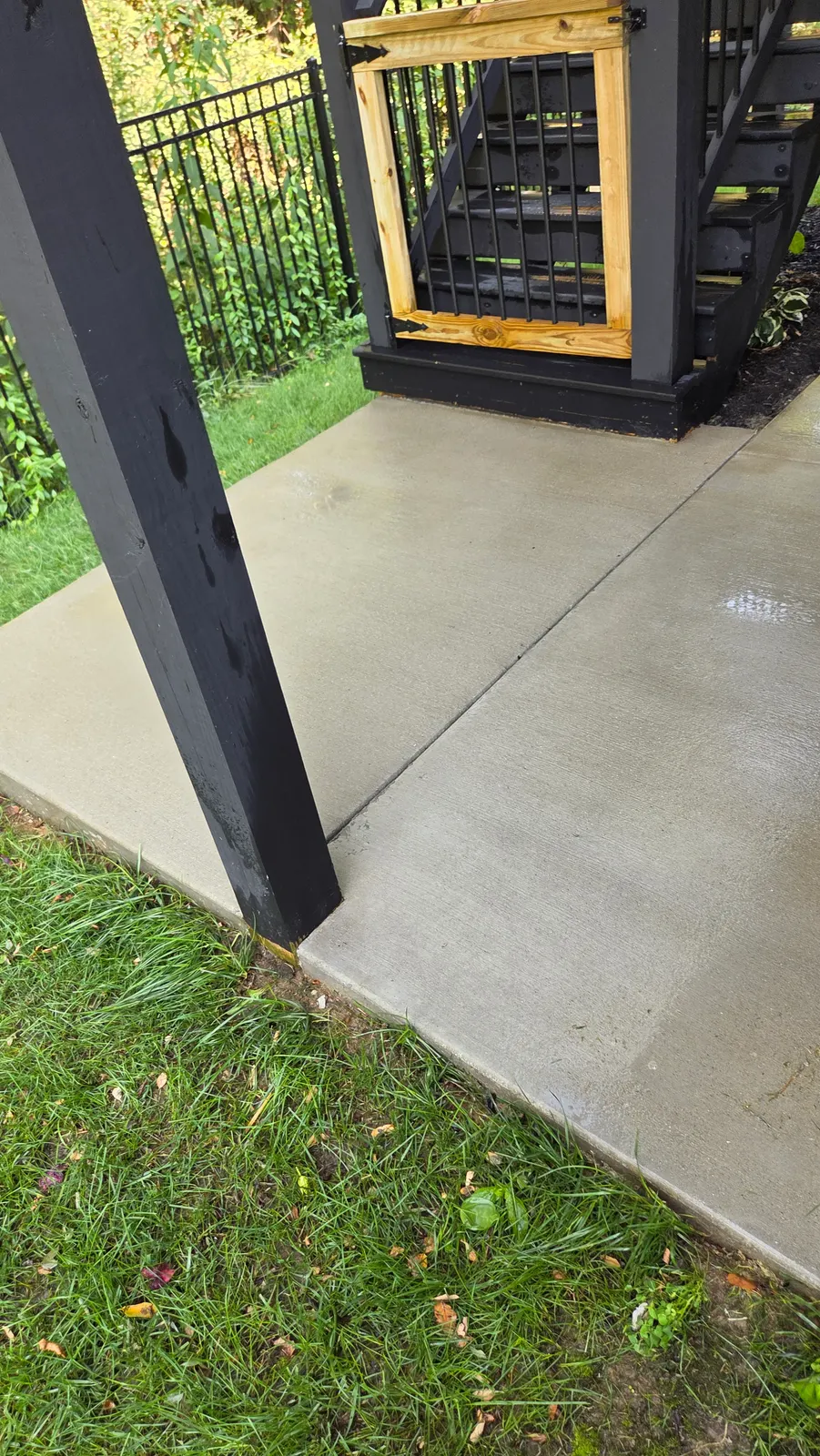 Clean light gray concrete patio beside a dark support post and a green lawn.