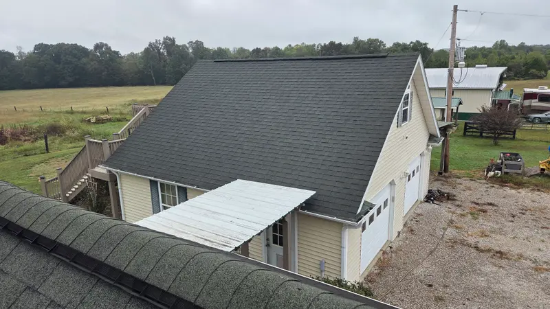 A detached garage with a dark shingle roof and a white metal awning roof, seen from a neighboring rooftop.