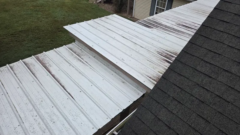 A white metal porch roof with dark rust-colored streaks running down the panels, next to dark shingles.