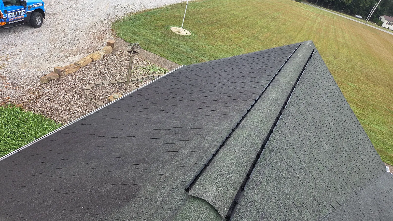 A shingle roof ridge with heavy dark streaking across the slope, above a lawn and gravel drive.