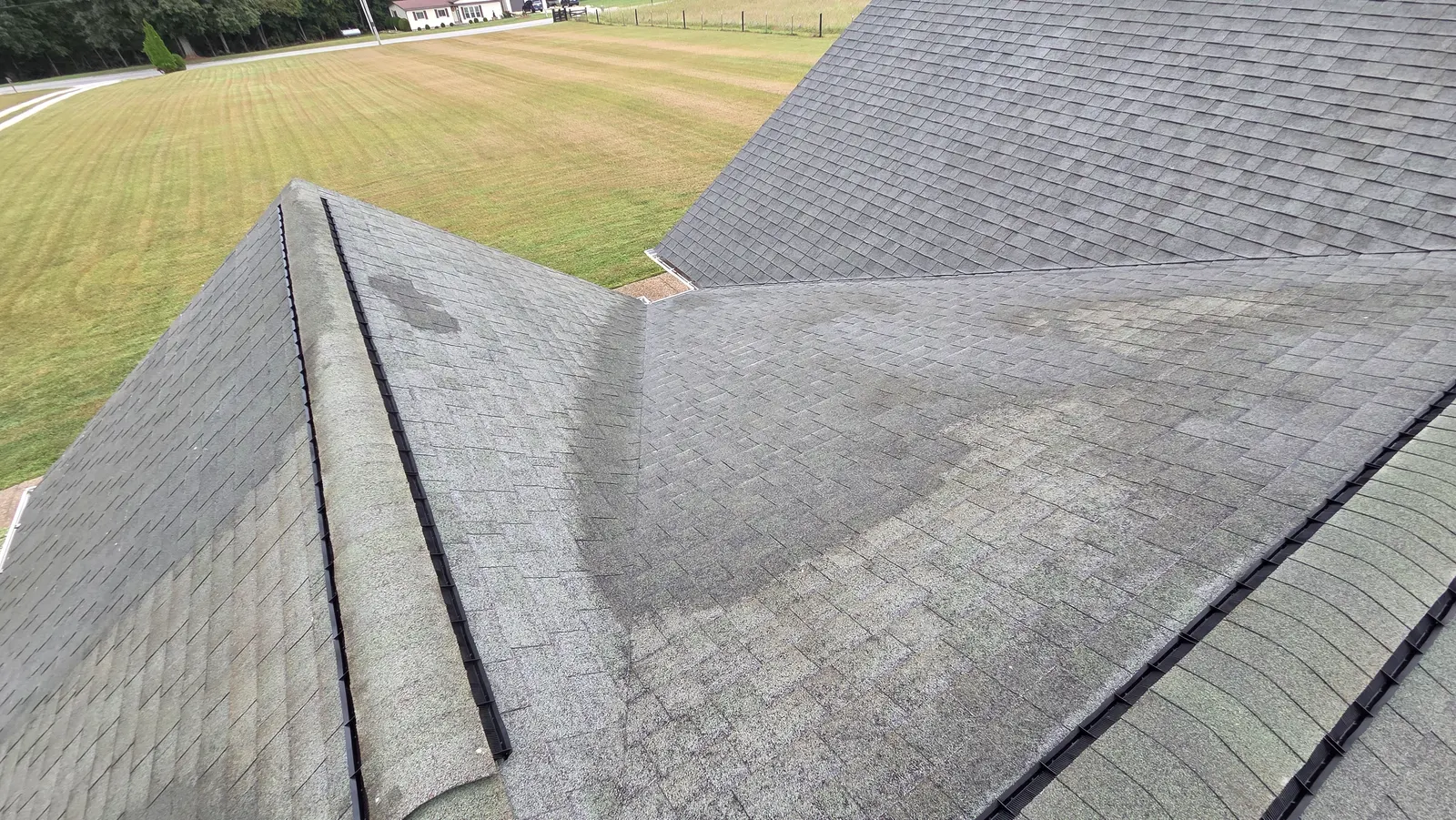 The same shingle roof partway through washing, with lighter cleaned shingles next to the darker untreated area.