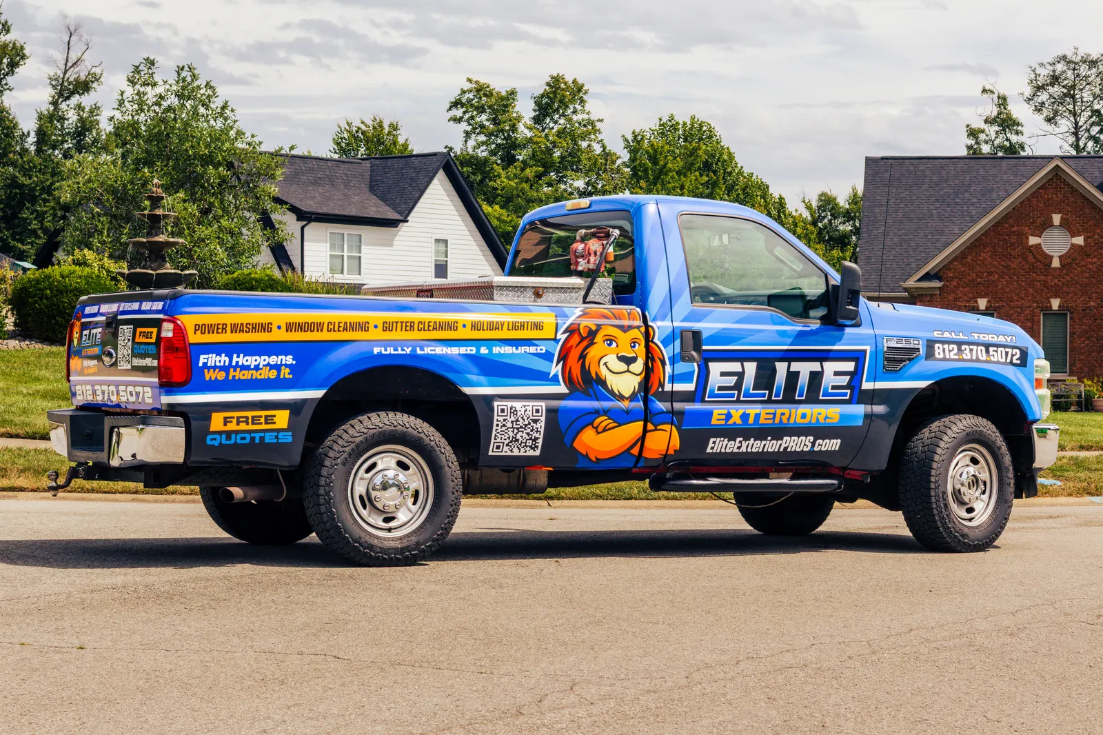 Side view of the blue wrapped Elite Exteriors pickup truck parked in a neighborhood, with the service list and phone number on the wrap.