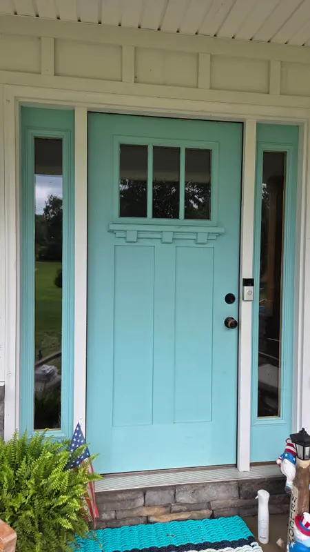 A teal front door with clean glass sidelights and door panes on a covered porch.