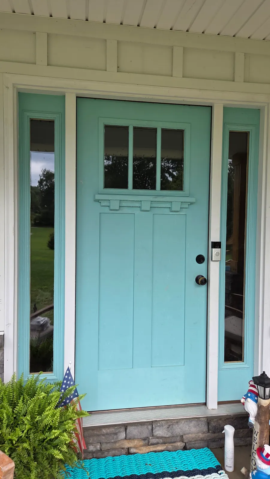 A teal front door with clean glass sidelights and door panes on a covered porch.