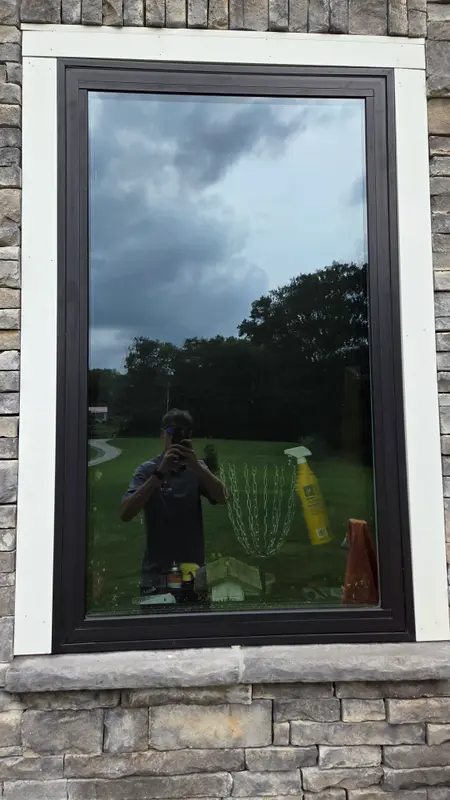 The same dark-framed picture window after cleaning, with clear glass reflecting the sky and yard.