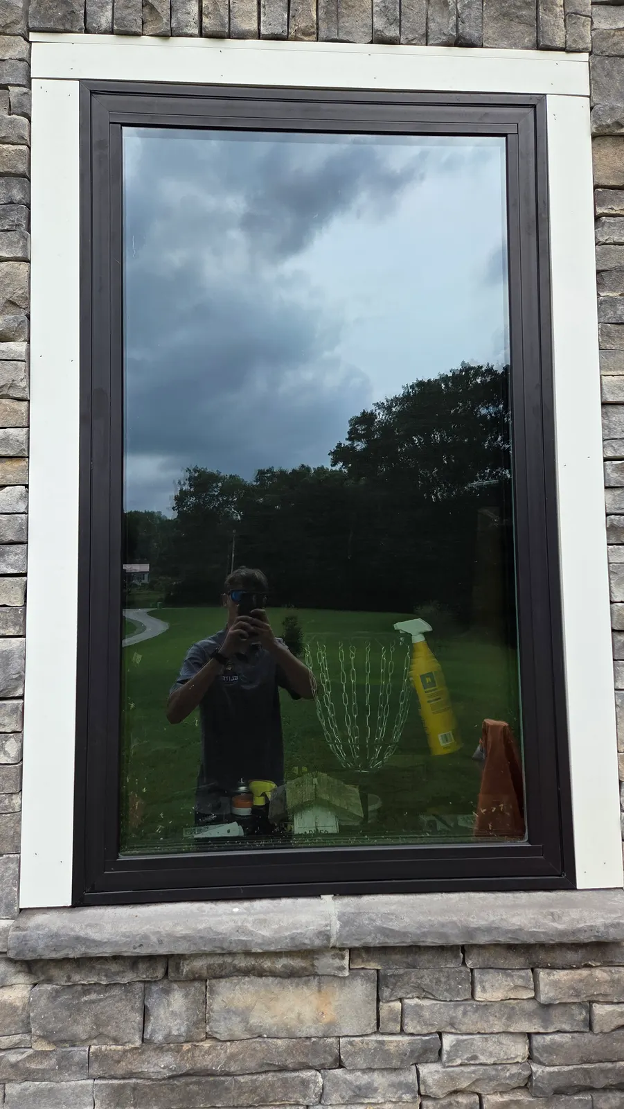The same dark-framed picture window after cleaning, with clear glass reflecting the sky and yard.