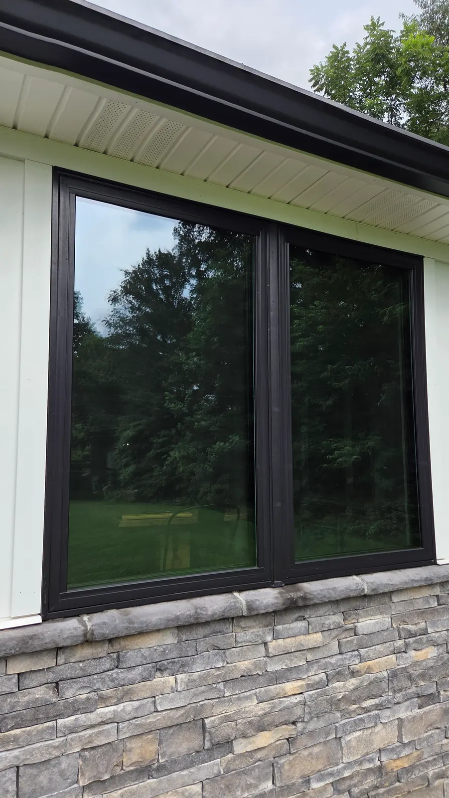 Clean dark-framed double window on a white board-and-batten house with stone veneer below.