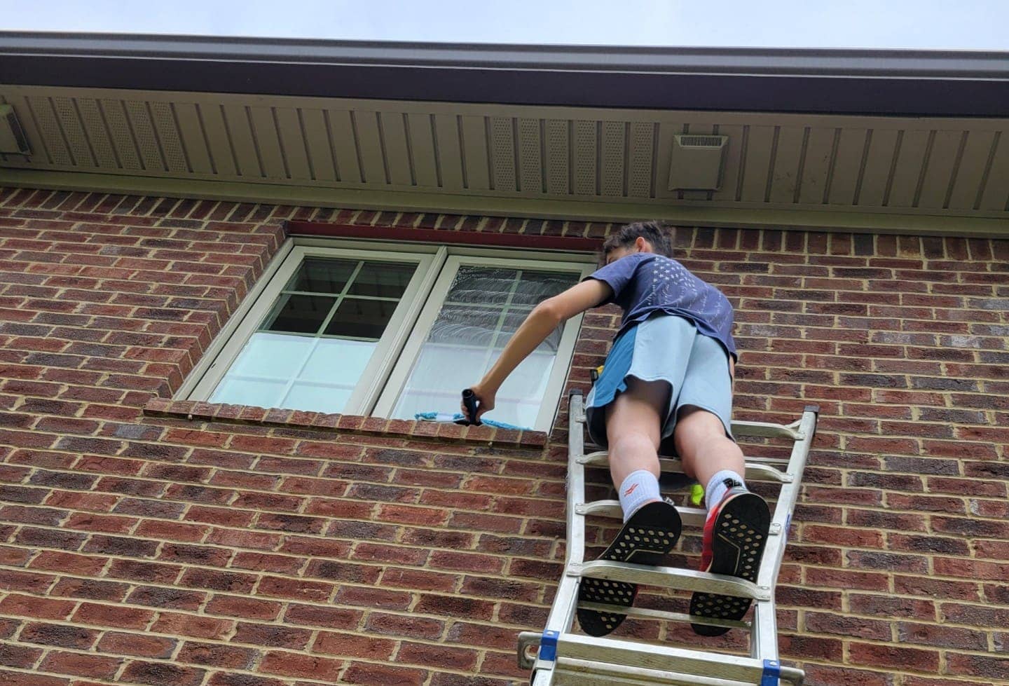 Elite Exteriors team member using a water-fed pole to clean second-story windows on a home in Southern Indiana
