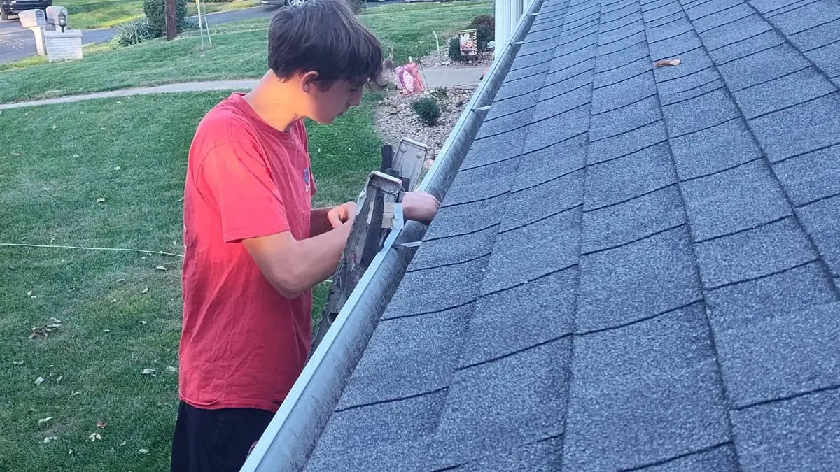 Technician hand cleaning leaves and debris from a home gutter in New Albany, Indiana
