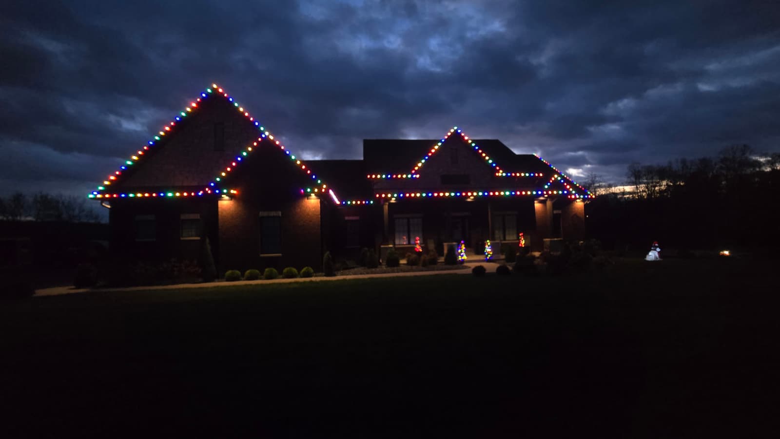 Brick home in Southern Indiana outlined in multicolor C9 Christmas lights under an evening sky