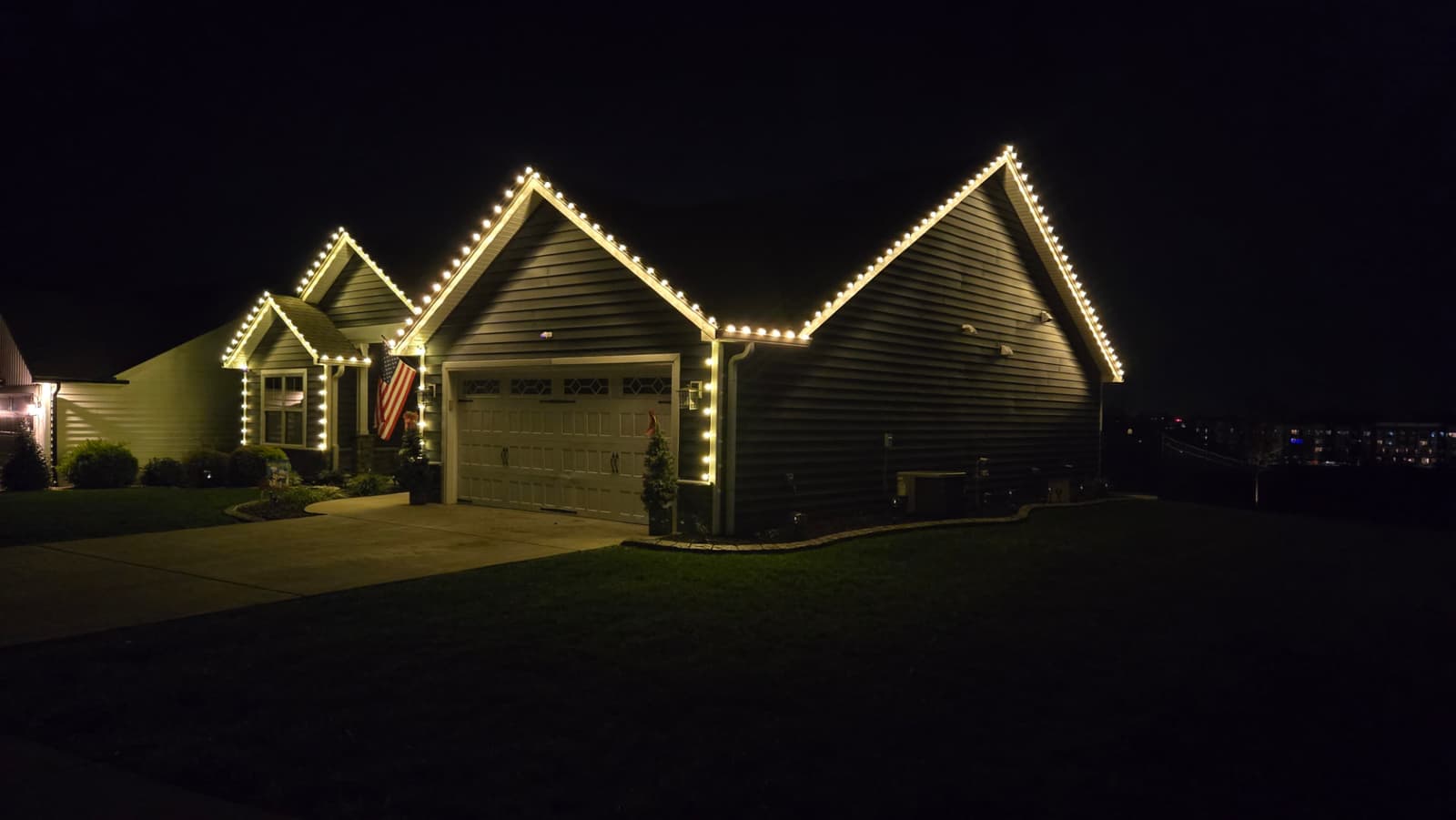 Two-car garage and roof peaks outlined in warm white C9 Christmas lights at night